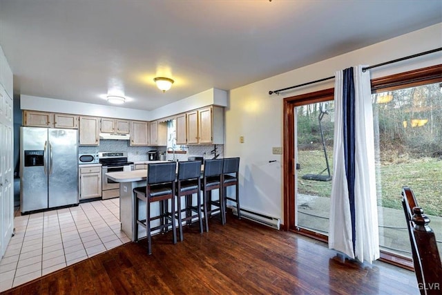 kitchen with appliances with stainless steel finishes, backsplash, light brown cabinetry, a breakfast bar, and hardwood / wood-style floors