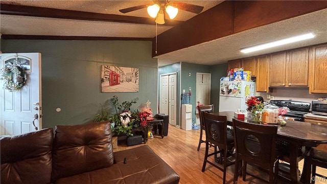 dining area featuring ceiling fan, lofted ceiling with beams, light hardwood / wood-style floors, and a textured ceiling