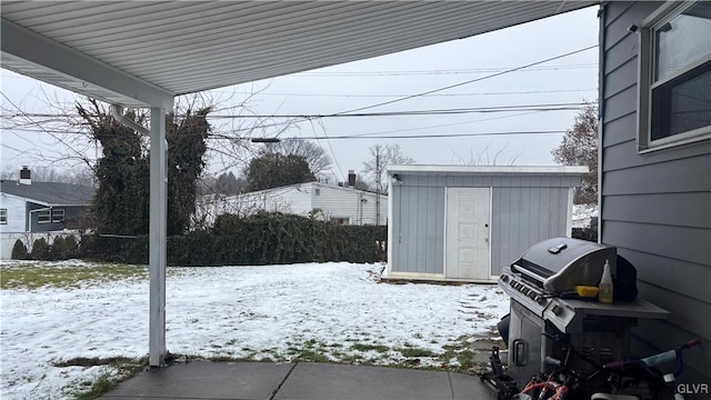 snow covered patio featuring a storage unit and a grill