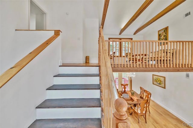 stairs featuring beamed ceiling, hardwood / wood-style flooring, and a chandelier