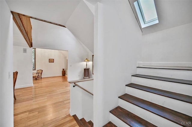 stairs with lofted ceiling with skylight and wood-type flooring