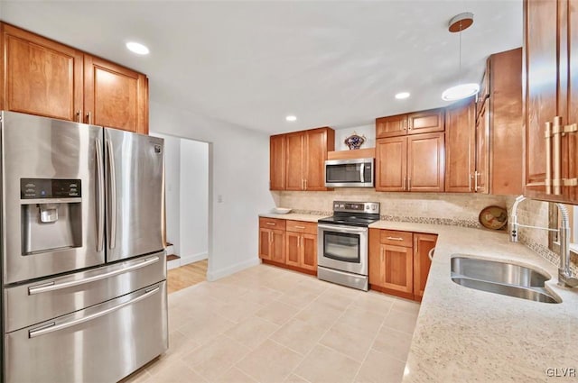 kitchen with sink, light stone counters, backsplash, pendant lighting, and appliances with stainless steel finishes