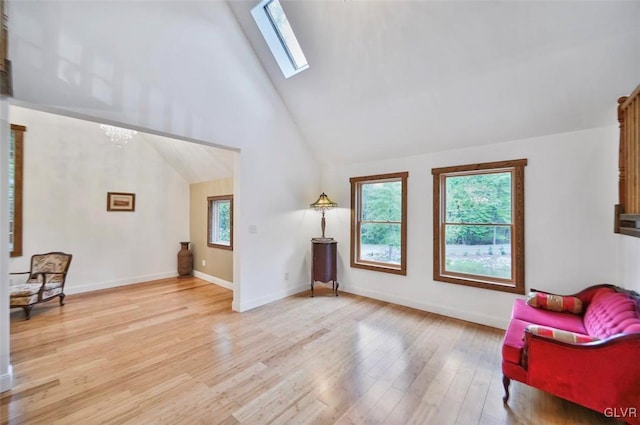 living area featuring an inviting chandelier, a skylight, high vaulted ceiling, and light hardwood / wood-style flooring