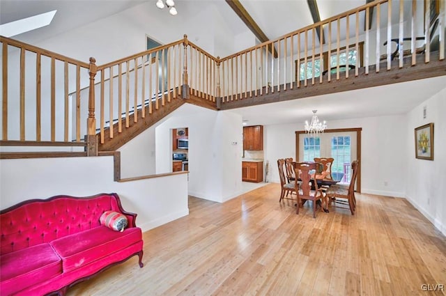 dining space featuring a skylight, light wood-type flooring, high vaulted ceiling, and a chandelier