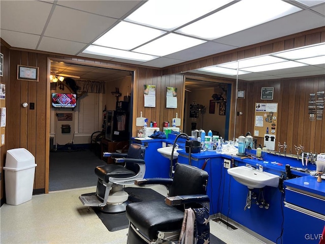 interior space with sink, ceiling fan, a paneled ceiling, and wood walls