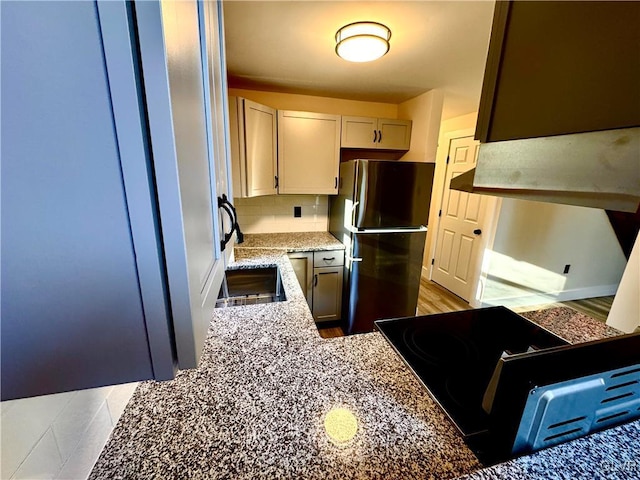 kitchen with stainless steel fridge, stove, light stone counters, and backsplash