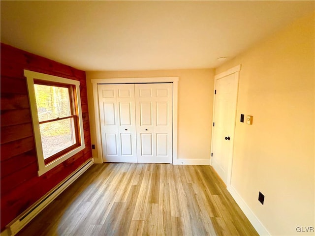 unfurnished bedroom featuring baseboard heating, a closet, and light hardwood / wood-style floors