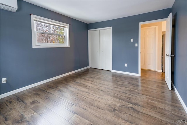 unfurnished bedroom with a wall mounted AC, a closet, and dark wood-type flooring