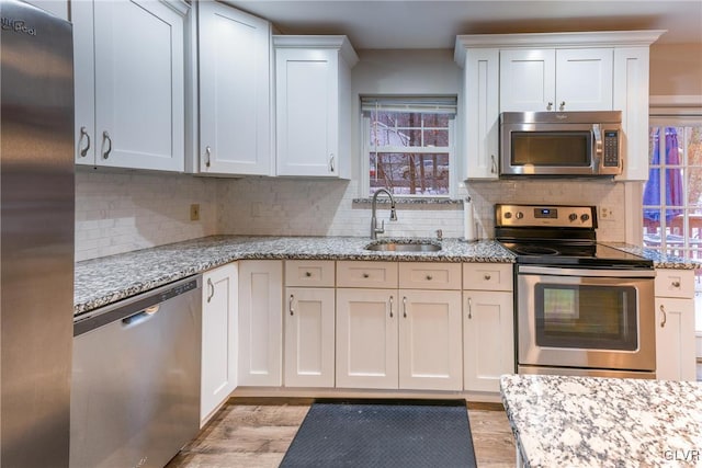 kitchen featuring decorative backsplash, appliances with stainless steel finishes, light stone counters, sink, and white cabinets