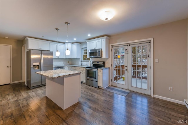 kitchen featuring light stone countertops, stainless steel appliances, pendant lighting, white cabinetry, and a kitchen island