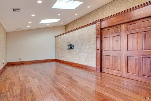 spare room featuring a skylight and light hardwood / wood-style flooring