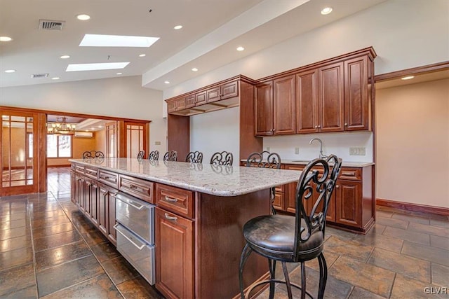 kitchen featuring light stone countertops, an inviting chandelier, a kitchen breakfast bar, lofted ceiling with skylight, and a kitchen island with sink