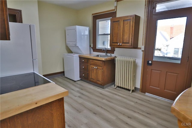 laundry area featuring radiator heating unit, light hardwood / wood-style flooring, stacked washer / drying machine, and sink