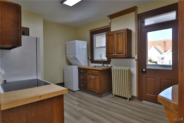 kitchen featuring radiator, sink, stacked washing maching and dryer, white fridge, and light hardwood / wood-style floors