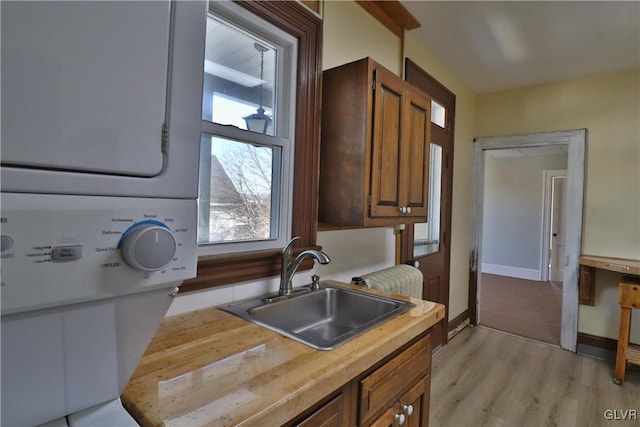 kitchen with stacked washing maching and dryer, sink, and light hardwood / wood-style flooring