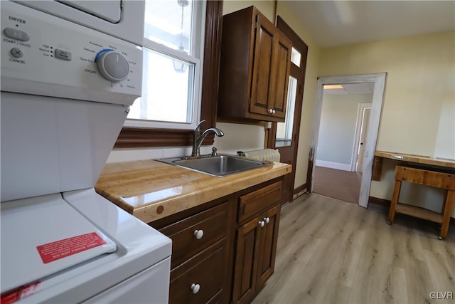 kitchen with dark brown cabinetry, light hardwood / wood-style flooring, stacked washer and clothes dryer, and sink