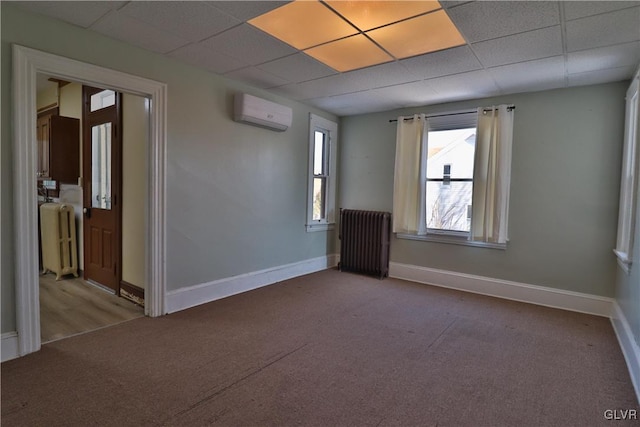 unfurnished room with carpet flooring, a drop ceiling, a wall mounted air conditioner, and radiator heating unit