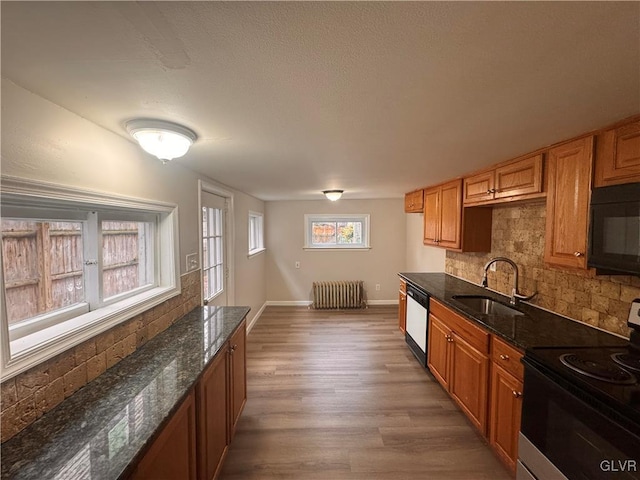 kitchen featuring sink, radiator heating unit, backsplash, dark stone counters, and black appliances