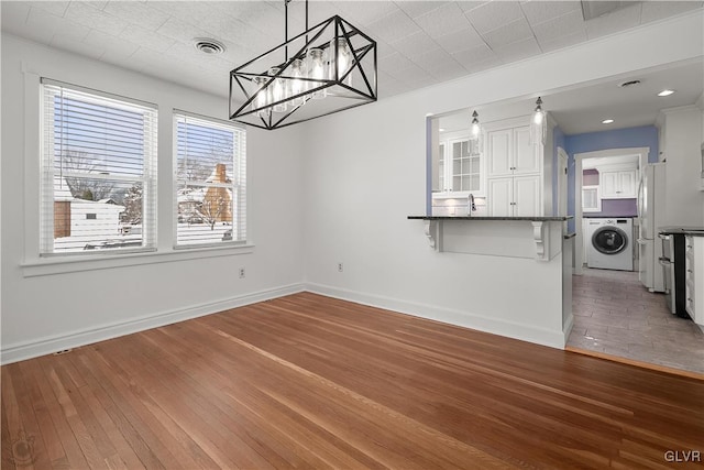 unfurnished dining area featuring sink, dark hardwood / wood-style flooring, a chandelier, and washer / dryer