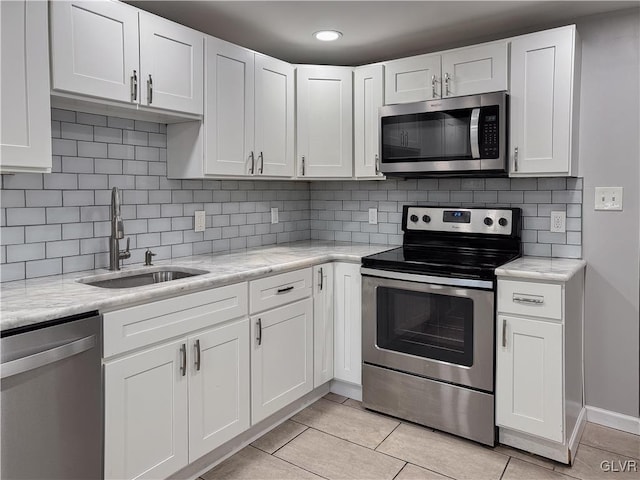 kitchen with appliances with stainless steel finishes, light tile patterned floors, white cabinetry, and sink