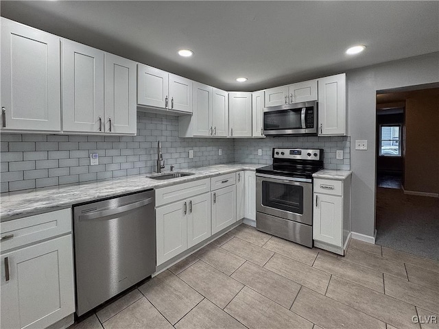 kitchen featuring light stone countertops, tasteful backsplash, stainless steel appliances, sink, and white cabinetry