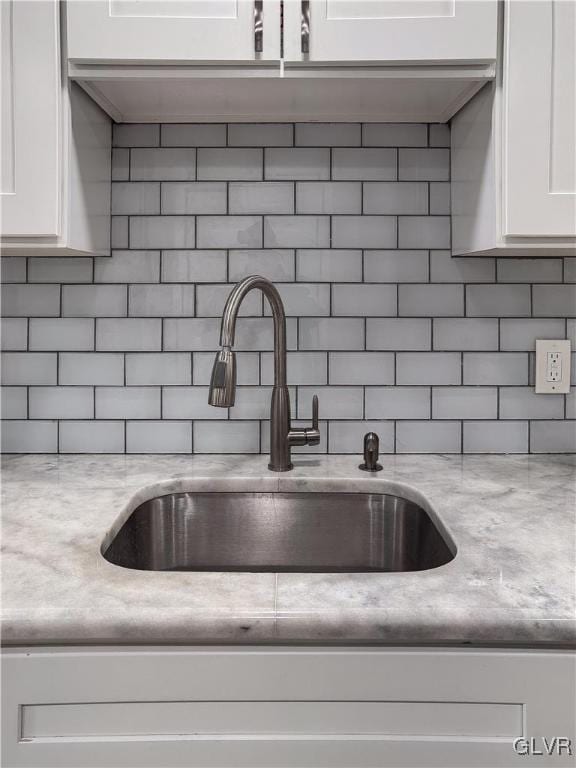 details featuring white cabinets, tasteful backsplash, light stone countertops, and sink