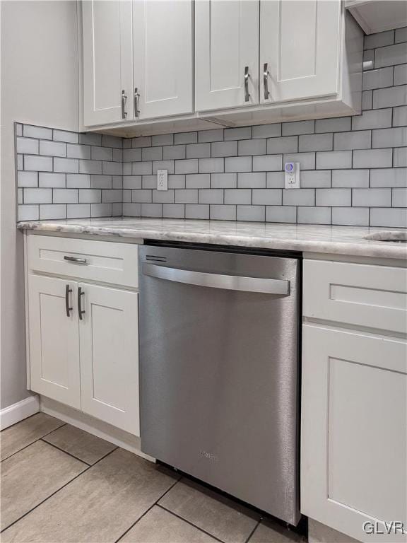 kitchen with white cabinets, light tile patterned floors, stainless steel dishwasher, and light stone countertops