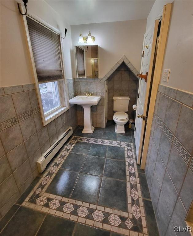 bathroom with a baseboard heating unit, sink, tile patterned flooring, toilet, and tile walls