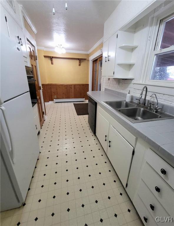 kitchen featuring wood walls, tile counters, white cabinets, and sink