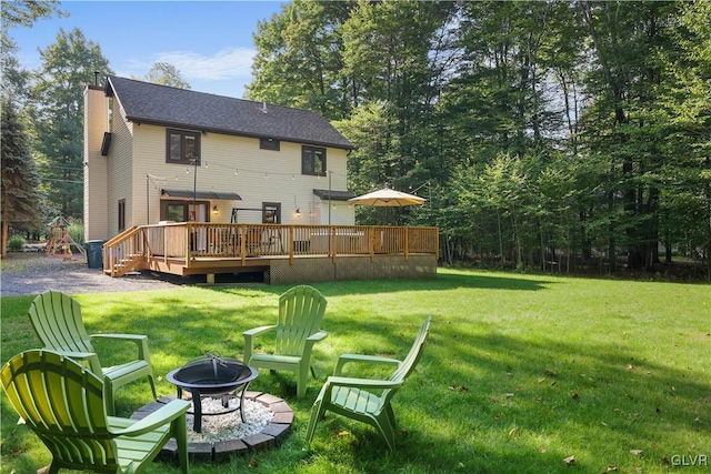 rear view of property with a lawn, a deck, and an outdoor fire pit