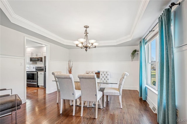 dining area with a tray ceiling, ornamental molding, dark wood-type flooring, and a notable chandelier