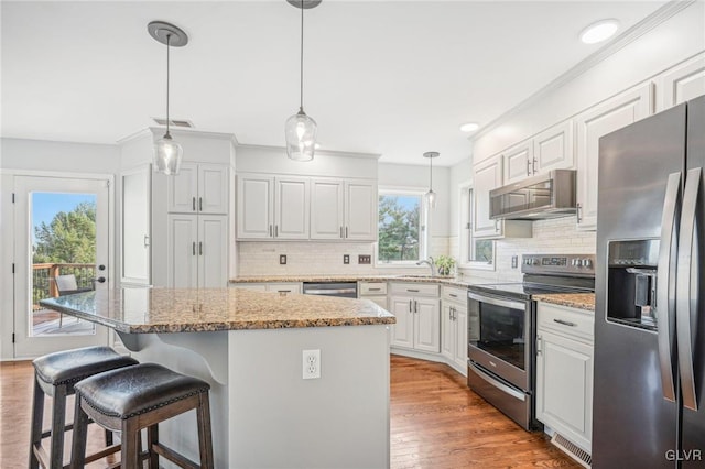 kitchen featuring white cabinetry, stainless steel appliances, light stone counters, pendant lighting, and a kitchen island