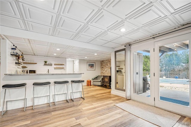 kitchen featuring a kitchen bar, kitchen peninsula, light stone countertops, and light hardwood / wood-style flooring