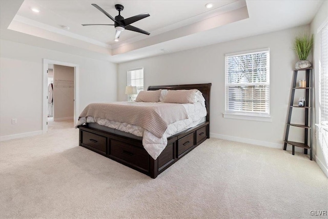 bedroom featuring a spacious closet, ceiling fan, a raised ceiling, light carpet, and a closet