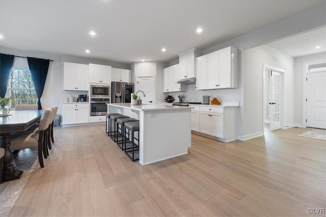 kitchen with a center island with sink, white cabinetry, a breakfast bar area, and appliances with stainless steel finishes