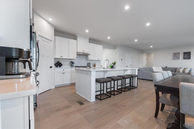 kitchen featuring a breakfast bar, a center island with sink, white cabinets, tasteful backsplash, and light hardwood / wood-style floors