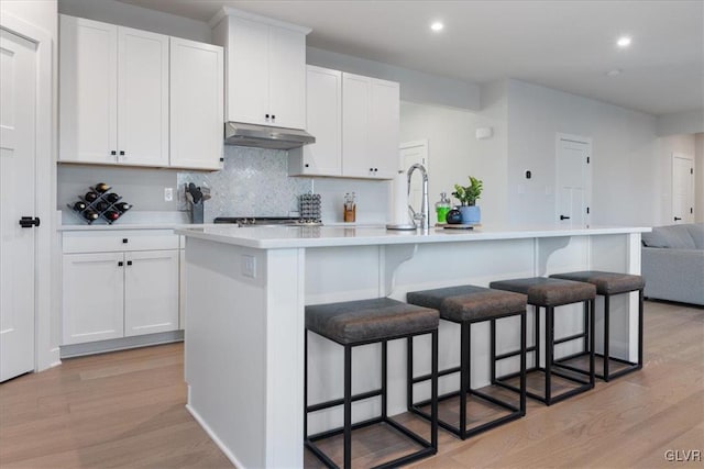 kitchen featuring backsplash, white cabinetry, an island with sink, and light hardwood / wood-style flooring