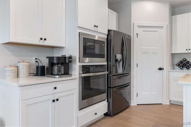 kitchen with appliances with stainless steel finishes, light wood-type flooring, and white cabinetry