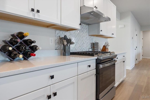 kitchen with light hardwood / wood-style flooring, light stone countertops, tasteful backsplash, stainless steel range oven, and white cabinetry