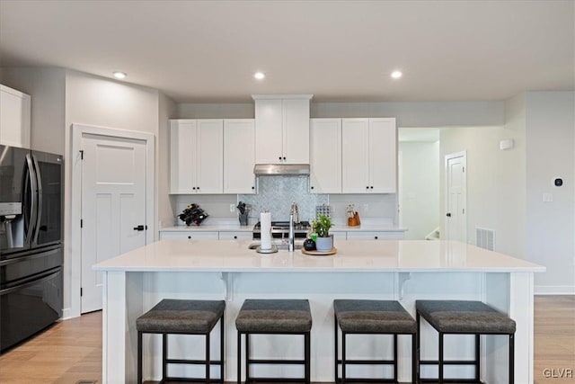 kitchen featuring white cabinets, black fridge with ice dispenser, a breakfast bar, and an island with sink