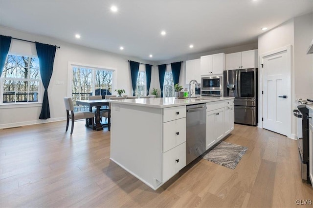 kitchen featuring light wood-type flooring, stainless steel appliances, a kitchen island with sink, sink, and white cabinets