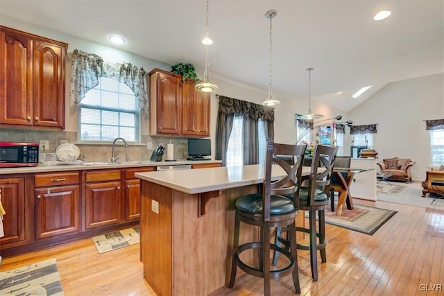 kitchen featuring a center island, hanging light fixtures, tasteful backsplash, light hardwood / wood-style floors, and vaulted ceiling