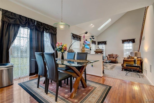 dining space featuring high vaulted ceiling, a skylight, and light hardwood / wood-style flooring