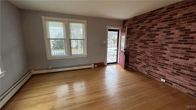 unfurnished room with baseboard heating, brick wall, and light hardwood / wood-style flooring