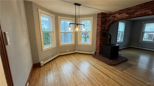 unfurnished dining area with wood-type flooring, a wood stove, brick wall, and a baseboard radiator