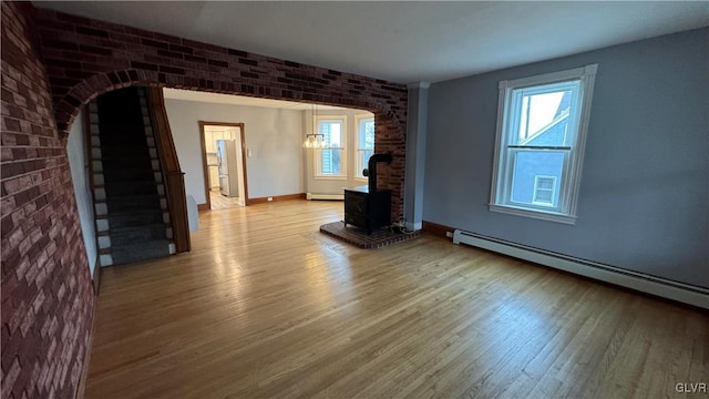 unfurnished living room featuring a wood stove, a baseboard heating unit, and brick wall