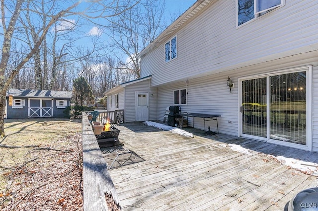 wooden terrace with a shed, a fire pit, and a grill