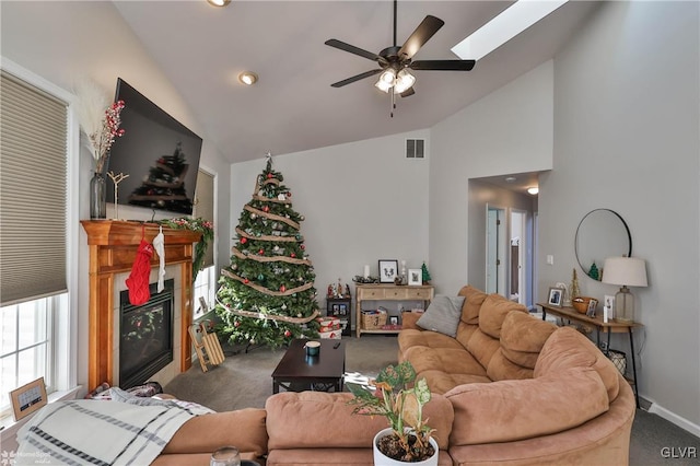 carpeted living room with ceiling fan and vaulted ceiling with skylight