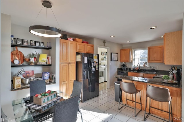 kitchen with black appliances, light tile patterned floors, sink, and a breakfast bar area