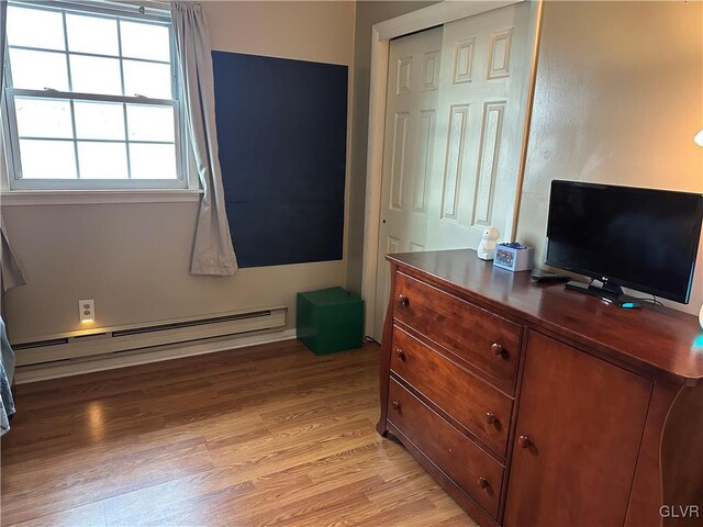 bedroom with a baseboard heating unit, light hardwood / wood-style flooring, and a closet